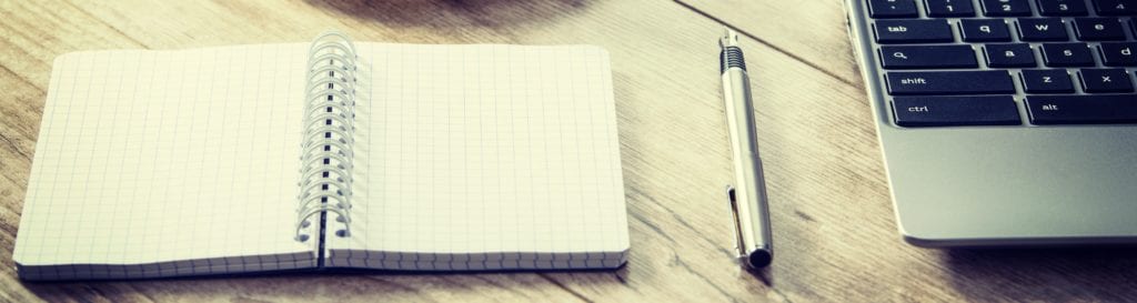 Blank notepad and a pen next to a laptop and coffee on a wooden vintage desk