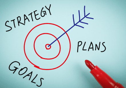 Target and arrow drawn in between the words 'strategy', 'plans', 'goals'