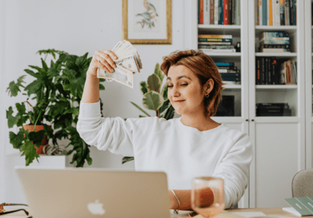 Woman working at laptop holding a wodge of cash